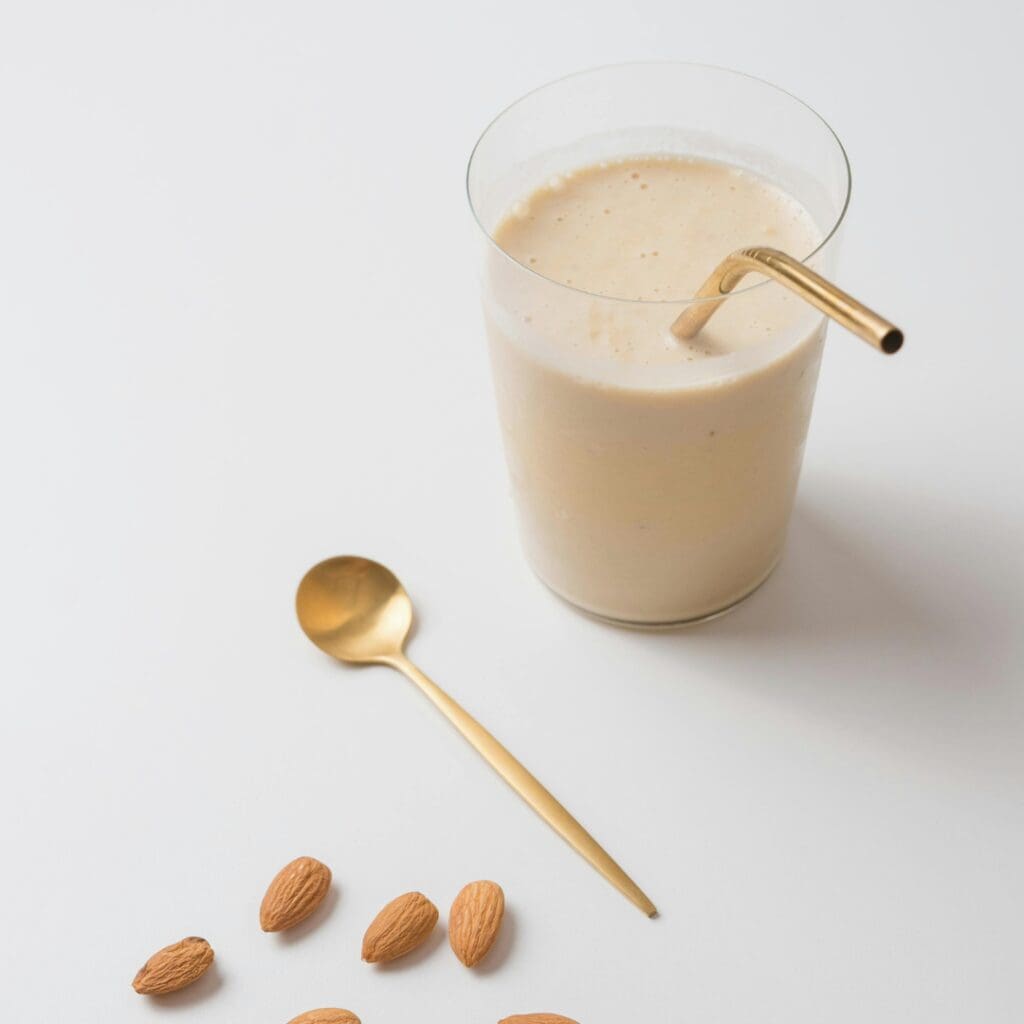 Meal replacement shake in a glass on a neutral background with almonds scattered around.