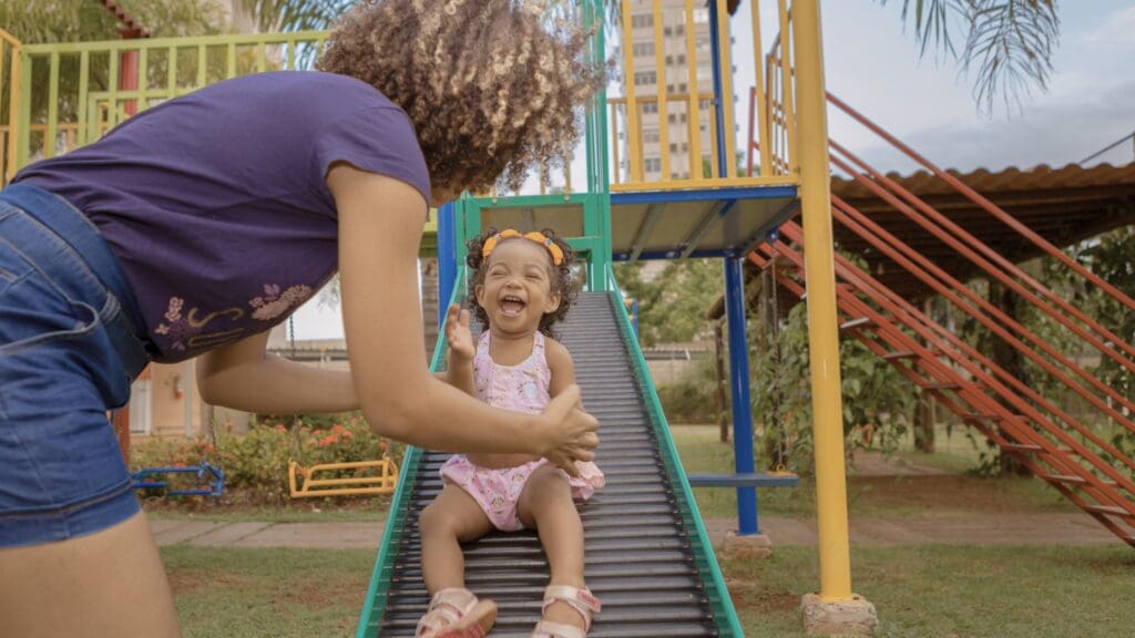 Woman and child playing on a park playground with the child laughing towards the camera.