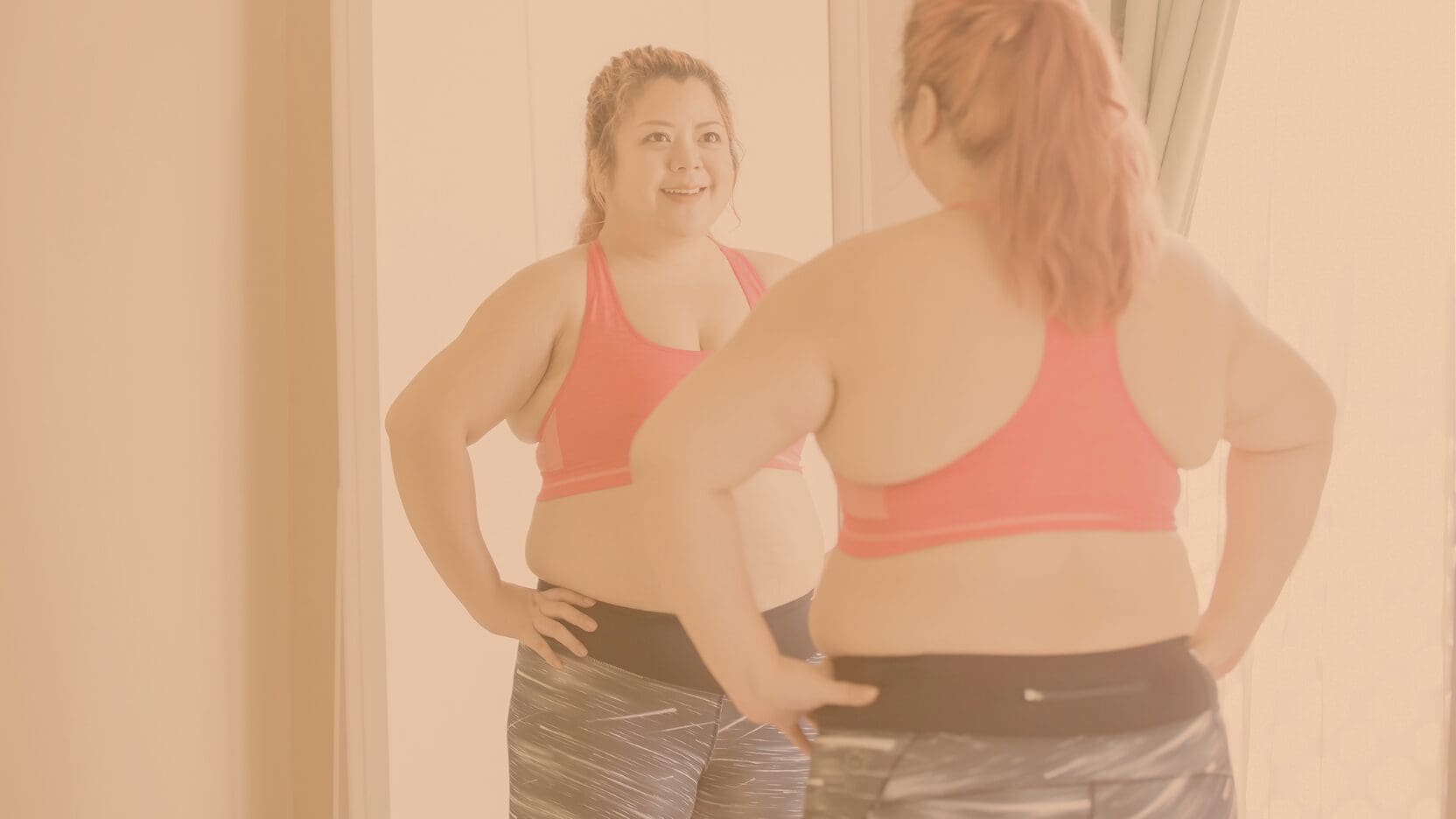 Woman smiling at herself in the mirror while wearing a workout outfit.